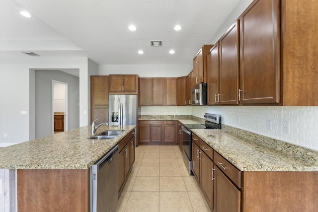 kitchen with sink, light tile patterned floors, an island with sink, appliances with stainless steel finishes, and tasteful backsplash