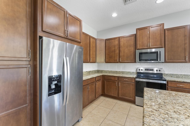 kitchen with light stone counters, light tile patterned floors, a textured ceiling, and appliances with stainless steel finishes