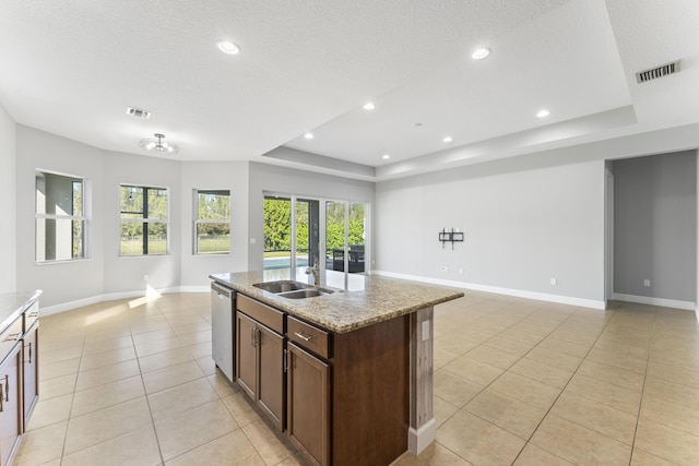 kitchen featuring dishwasher, a center island with sink, sink, a tray ceiling, and light stone counters