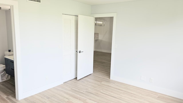 unfurnished bedroom with ensuite bathroom, a closet, and light hardwood / wood-style flooring