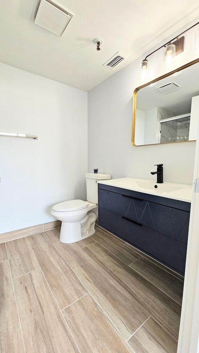 bathroom with hardwood / wood-style floors, vanity, toilet, and a shower with door