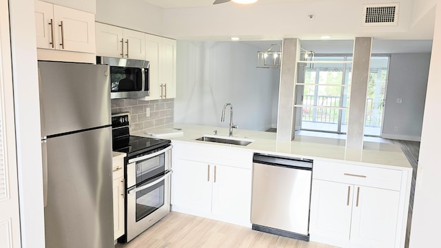 kitchen featuring decorative backsplash, light wood-type flooring, stainless steel appliances, sink, and white cabinetry