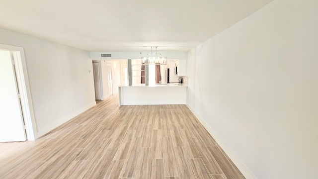 unfurnished living room featuring a chandelier and light wood-type flooring