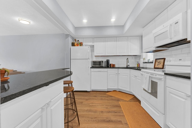 kitchen with white appliances, a kitchen breakfast bar, decorative backsplash, light wood-type flooring, and white cabinetry