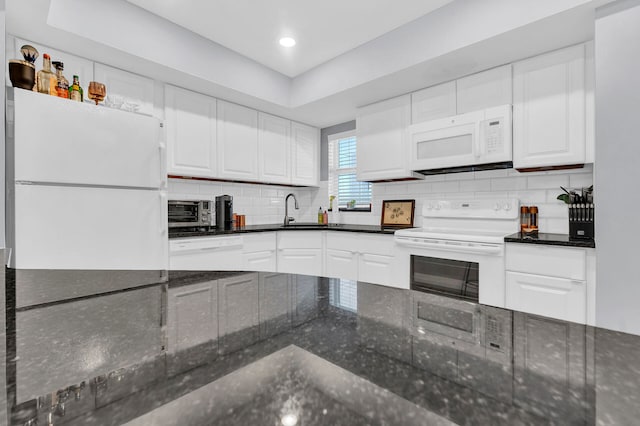 kitchen featuring white appliances, dark stone counters, white cabinets, sink, and decorative backsplash