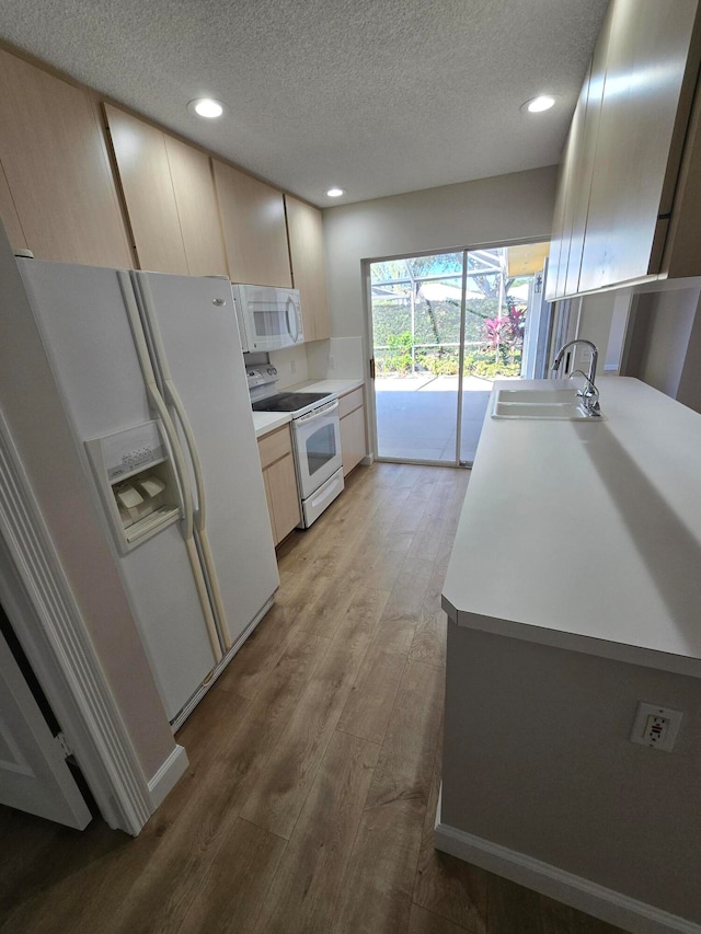 kitchen with light brown cabinetry, light wood-type flooring, white appliances, a textured ceiling, and sink