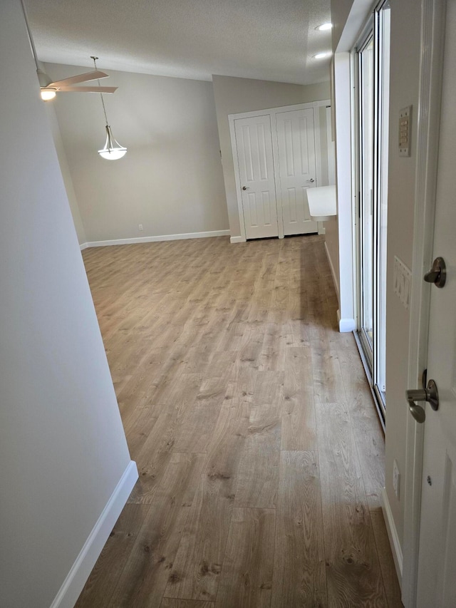 corridor featuring lofted ceiling, a healthy amount of sunlight, light wood-type flooring, and a textured ceiling