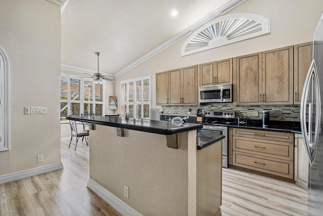 kitchen featuring lofted ceiling, a breakfast bar, backsplash, stainless steel appliances, and light wood-type flooring