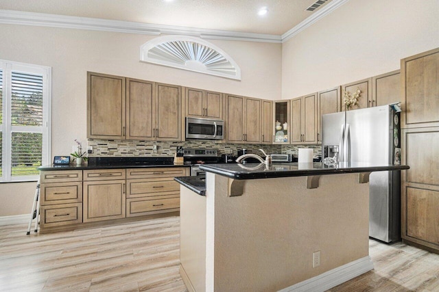 kitchen with a breakfast bar, tasteful backsplash, an island with sink, ornamental molding, and stainless steel appliances