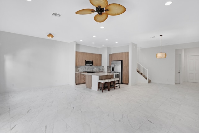 kitchen with ceiling fan, tasteful backsplash, pendant lighting, a kitchen island, and appliances with stainless steel finishes