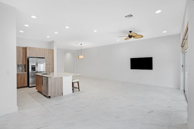 kitchen with pendant lighting, a breakfast bar, a kitchen island with sink, ceiling fan, and stainless steel appliances