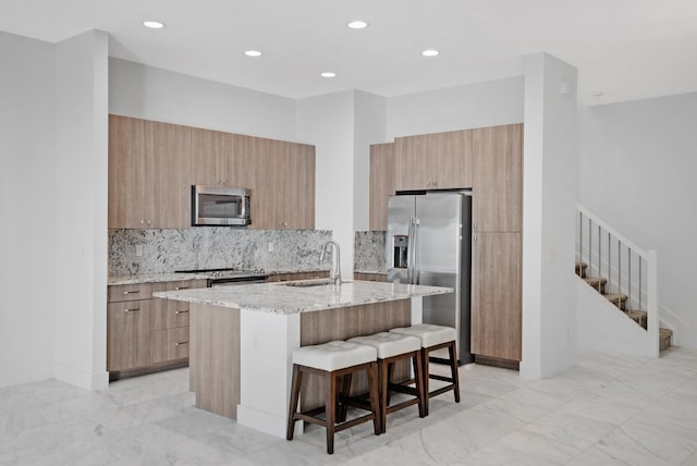 kitchen featuring a center island with sink, sink, a breakfast bar area, light stone countertops, and stainless steel appliances