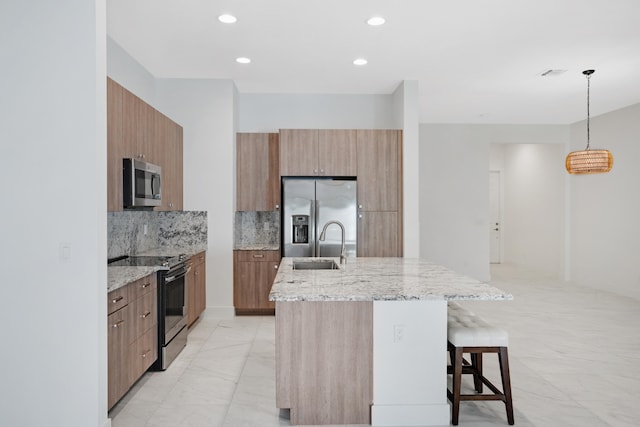 kitchen with light stone countertops, hanging light fixtures, stainless steel appliances, a kitchen island with sink, and a breakfast bar