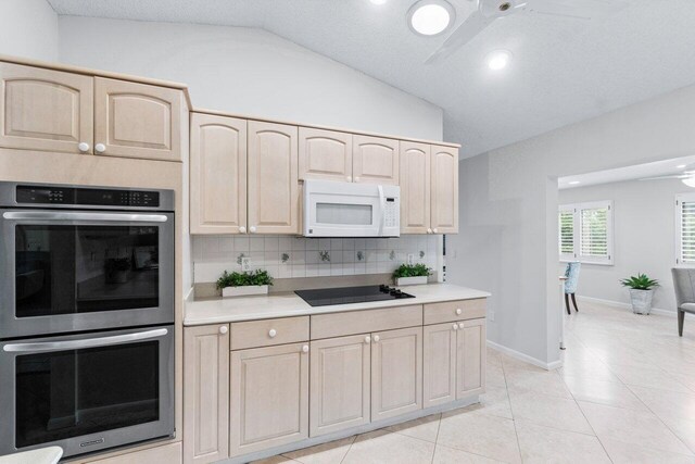 kitchen with light brown cabinets, black electric cooktop, double oven, and vaulted ceiling