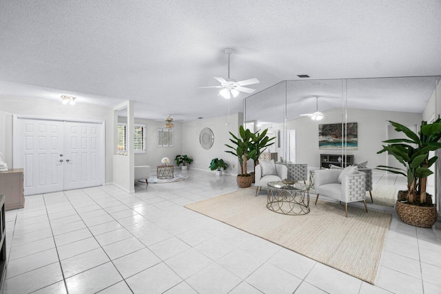 living room featuring a textured ceiling, ceiling fan, light tile patterned flooring, and vaulted ceiling