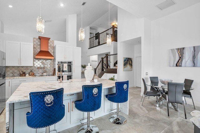 kitchen with a kitchen island with sink, a breakfast bar, white cabinetry, and pendant lighting