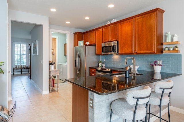 kitchen featuring washer and clothes dryer, sink, dark stone countertops, appliances with stainless steel finishes, and kitchen peninsula