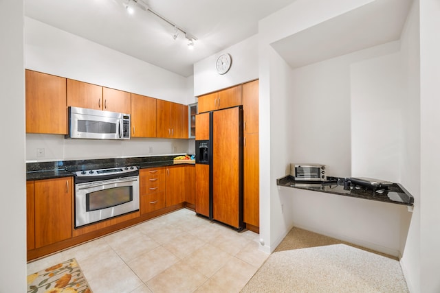 kitchen featuring dark stone countertops, light tile patterned flooring, rail lighting, and stainless steel appliances