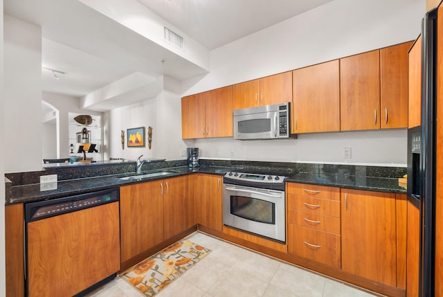 kitchen with sink, light tile patterned floors, dark stone counters, and appliances with stainless steel finishes