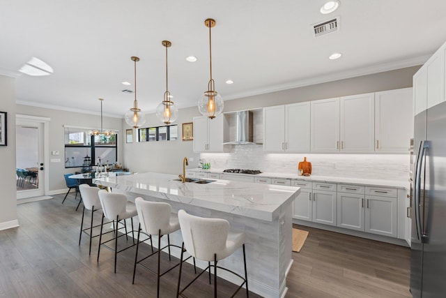 kitchen with a center island with sink, white cabinetry, wall chimney range hood, and stainless steel appliances