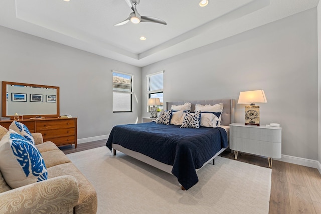 bedroom with hardwood / wood-style floors, a tray ceiling, and ceiling fan