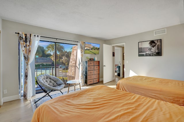 bedroom featuring a textured ceiling, access to outside, and light hardwood / wood-style flooring