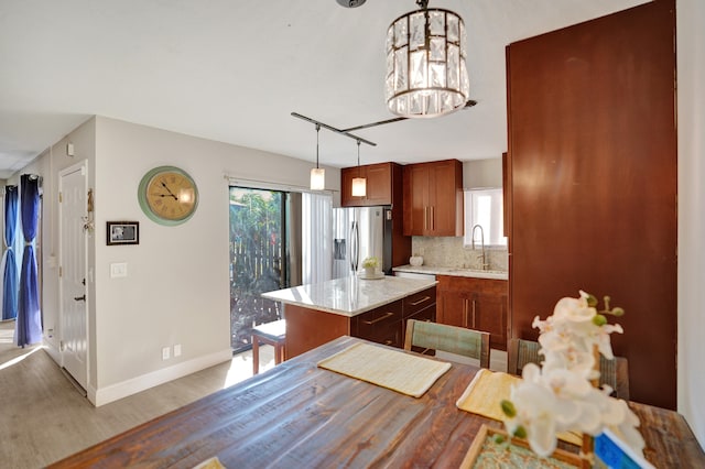 kitchen featuring a center island, hanging light fixtures, stainless steel refrigerator with ice dispenser, backsplash, and light wood-type flooring