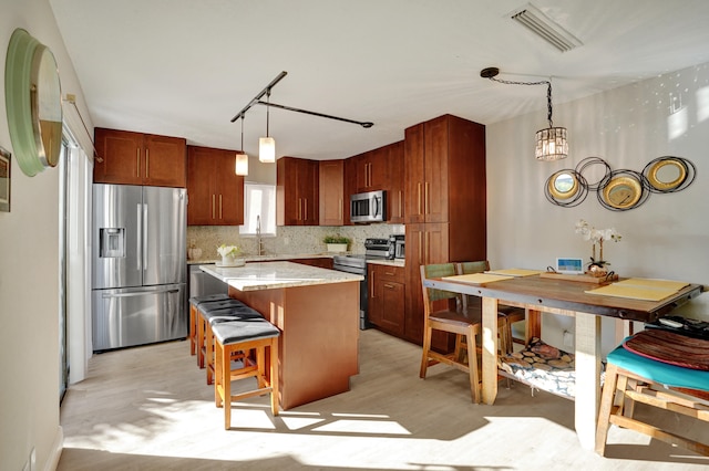 kitchen featuring a center island, hanging light fixtures, stainless steel appliances, decorative backsplash, and light wood-type flooring