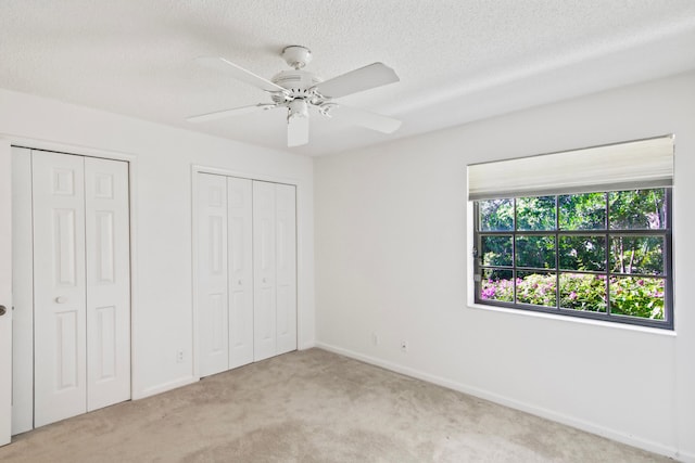 unfurnished bedroom featuring a textured ceiling, light colored carpet, ceiling fan, and multiple closets