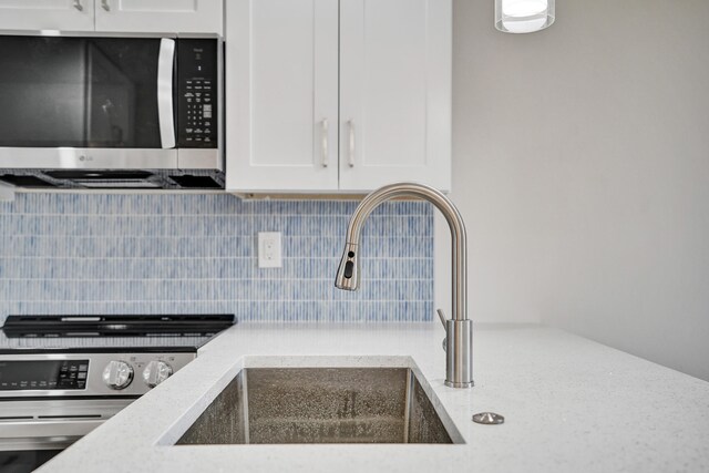 kitchen with light stone countertops, backsplash, stainless steel appliances, sink, and white cabinets