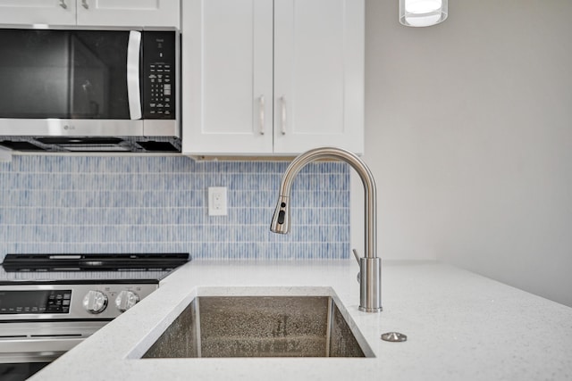 kitchen featuring stainless steel microwave, a sink, decorative backsplash, white cabinetry, and light stone countertops