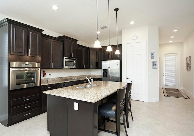 kitchen with a kitchen island with sink, sink, dark brown cabinets, light stone counters, and stainless steel appliances