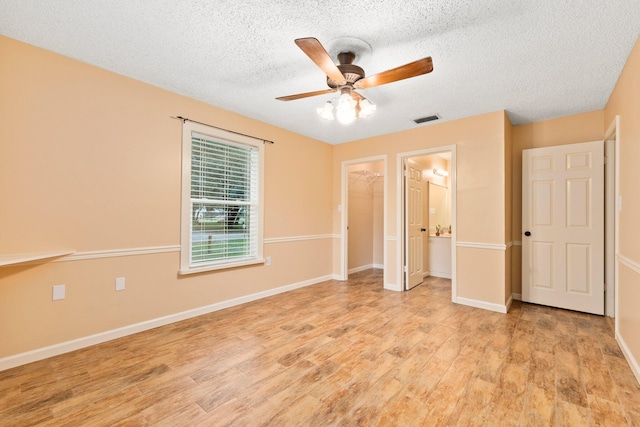 unfurnished bedroom with ceiling fan, a walk in closet, a textured ceiling, and light hardwood / wood-style flooring