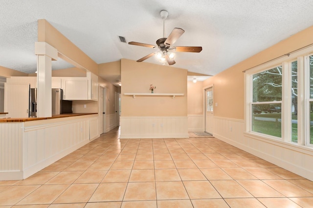 unfurnished living room featuring a textured ceiling, ceiling fan, light tile patterned flooring, and lofted ceiling