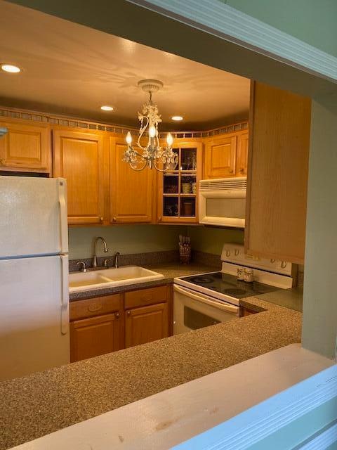 kitchen featuring white appliances, decorative light fixtures, a notable chandelier, and sink