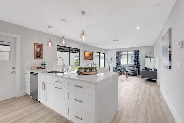 kitchen featuring light wood-type flooring, stainless steel dishwasher, sink, white cabinetry, and hanging light fixtures