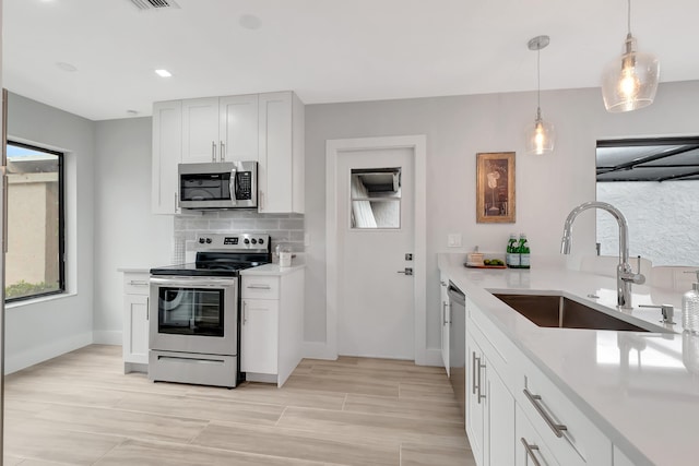 kitchen featuring pendant lighting, sink, tasteful backsplash, white cabinetry, and stainless steel appliances