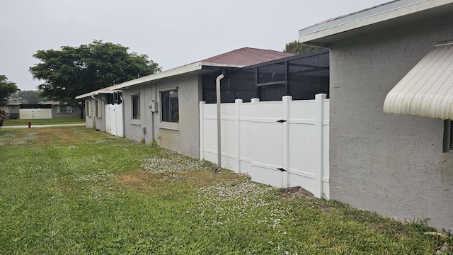 view of side of home featuring glass enclosure and a lawn