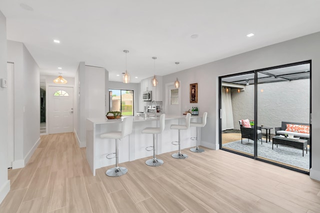 kitchen featuring white cabinetry, kitchen peninsula, decorative light fixtures, a breakfast bar, and appliances with stainless steel finishes