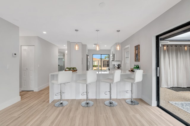 kitchen with a breakfast bar area, kitchen peninsula, white cabinetry, and hanging light fixtures