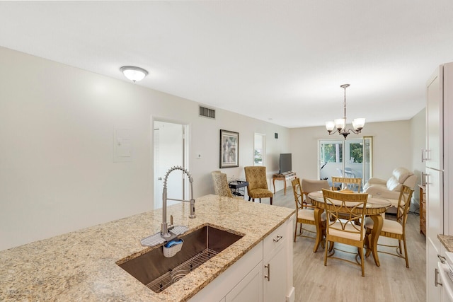 kitchen featuring pendant lighting, white cabinets, sink, light hardwood / wood-style flooring, and light stone countertops