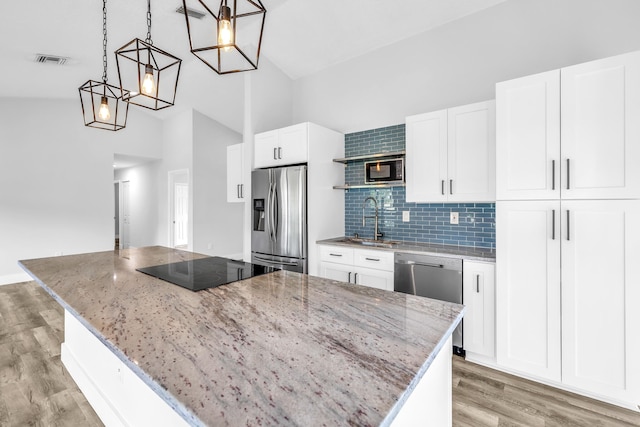 kitchen with light stone countertops, stainless steel appliances, decorative light fixtures, white cabinets, and a kitchen island