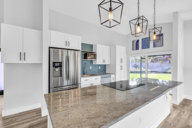 kitchen featuring light stone counters, stainless steel refrigerator with ice dispenser, decorative light fixtures, black electric cooktop, and white cabinets