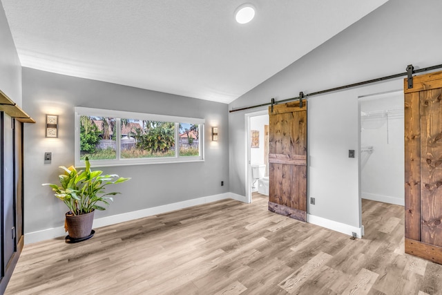 unfurnished bedroom with a barn door, light wood-type flooring, lofted ceiling, and a closet