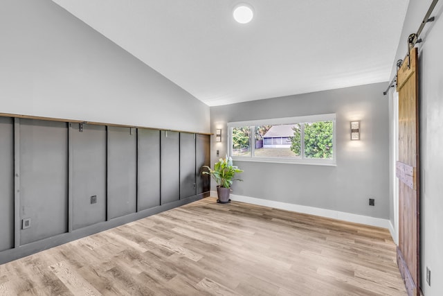 empty room with a barn door, light hardwood / wood-style floors, and lofted ceiling