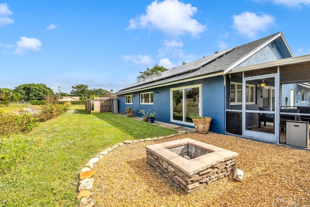 back of house featuring solar panels, an outdoor fire pit, a lawn, and a sunroom