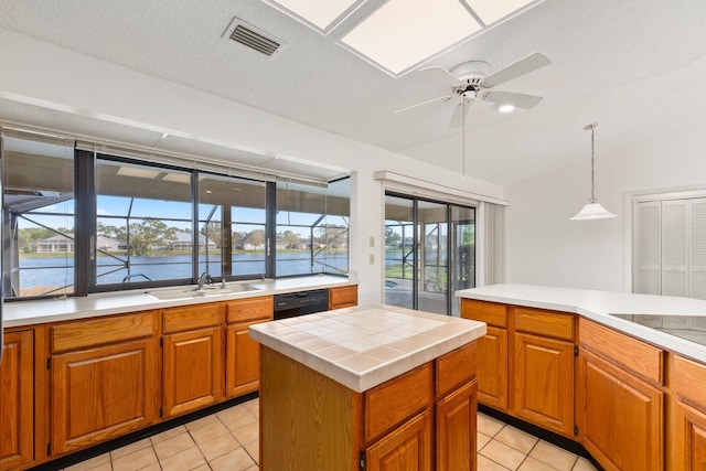 kitchen featuring sink, black dishwasher, light tile patterned flooring, decorative light fixtures, and a water view