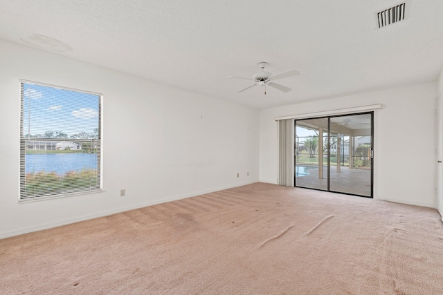 empty room with ceiling fan, a water view, light colored carpet, and a textured ceiling