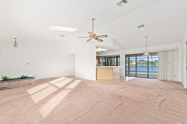 unfurnished living room featuring ceiling fan, a water view, light carpet, and a skylight