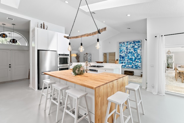 kitchen featuring white cabinetry, a kitchen bar, an island with sink, pendant lighting, and appliances with stainless steel finishes